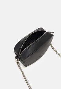 Černá kožená crossbody taška s texturovaným povrchem, zipovým uzávěrem a řetízkovým popruhem. V jednom rohu vygravírované logo, obdélníkový tvar.