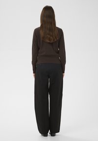 Barna, testhezálló pulóver hosszú ujjakkal és fekete, szárbő szárú nadrág. A ruházat sima textúrájú és egyszerű kialakítású.