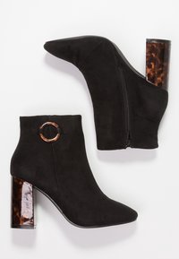 Botas de tobillo de ante negro con puntera afilada, cierre lateral de cremallera y un tacón grueso de carey brillante. Cuenta con un acento de hardware en forma circular.