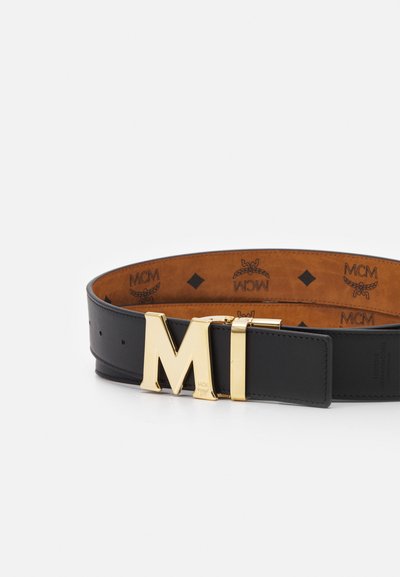 Svart läderbälte med en guldmetallspänne som har bokstäverna "MI." Inuti finns en brun läderfoder präglad med "MCM"-logotypen.