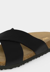 Μαύρο σανδάλι slip-on με φαρδιές σταυρωτές λουρίδες, φελλό πάτο και μαύρη ραβδωτή σόλα, σχεδιασμένο για καθημερινή χρήση.