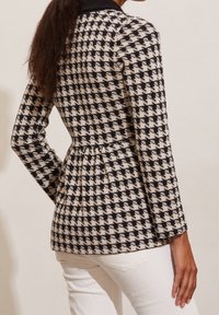 Black and white houndstooth patterned jacket with a fitted waist and long sleeves, featuring a black collar and textured fabric.