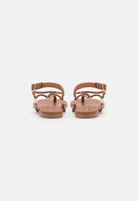 Sandales plates marron avec des brides tressées, des boucles réglables et une semelle en cuir lisse. Design minimaliste, dos ouvert et petit talon.