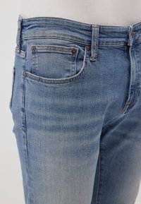 Light blue denim jeans featuring a five-pocket design, faded sections, and brass fixtures at the waistband and pockets.