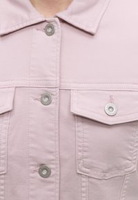 Μπροστινή όψη ανοιχτό ροζ τζιν μπουφάν με ασημένια κουμπιά και δύο τσεπάκια με καπάκι, εμφανίζοντας το γιακά και τις λεπτομέρειες ραφής.
