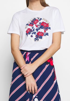 Camiseta de algodón blanca con estampado floral en rojo y azul marino, con lettering dorado, combinada con una falda azul marino con rayas rosas y patrones florales.