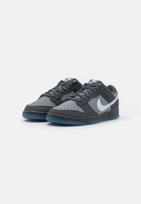Nike sneakers in black and gray, featuring a perforated toe, blue sole, and white swoosh logo, with flat laces and padded collar.