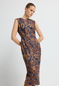 Ärmlös, figurnära klänning i mörkblått med guld- och bruna blommönster. Har en hög halsringning och sidofickor, tillverkad av mjukt tyg.