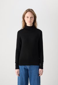 Svart polokrage i mjukt strikkmaterial, med långa ärmar och ribbade manschetter, kombinerad med ljusblå vida jeans.