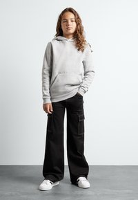 Grå huvtröja med framficka, kombinerad med lösa svarta cargobyxor med sidofickor och vita sneakers.