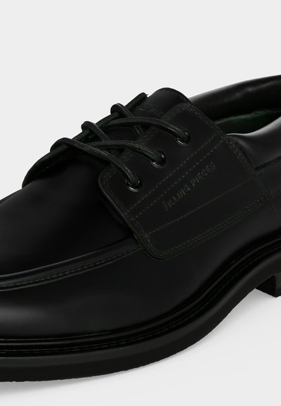 Chaussure montante en cuir noir avec bout arrondi, coutures visibles et nom de marque en relief sur le côté, présentée sur un fond uni.