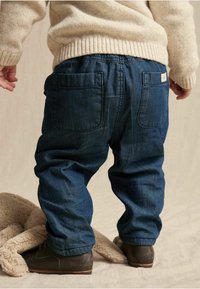 Jeans i mörkblått med resårmidja och två bakfickor. Tyget verkar mjukt, i kombination med en ljus färgad stickad tröja.