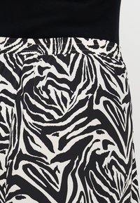 Svart og hvitt zebra-mønstrede stoff med en rynket elastisk midje, med iøjnefallende, bølgende striper og en glatt tekstur.