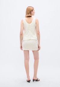 Σετ από λευκό αμάνικο τοπ με υφή και μίνι φούστα, με στρογγυλή πλάτη, φτιαγμένο από μαλακό ύφασμα με διακριτική λάμψη, συνδυασμένο με μαύρες γόβες.