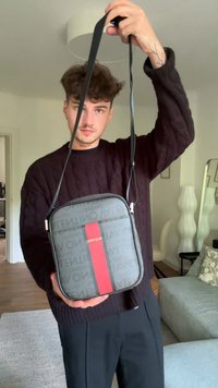 Borsa a tracolla nera realizzata in tessuto stampato, caratterizzata da una striscia rossa audace. Forma rettangolare con chiusura a zip e tracolla regolabile.