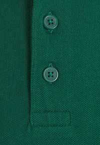 Gros plan sur un tissu tricoté vert avec deux boutons Levi's vert foncé et des détails de couture visibles.