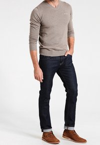 Beige V-ringad tröja, mörka jeans i denim med uppvikta benslut, och bruna ank stövlar. Tröjan har ribbade muddar och nederkant, avslappnad passform.