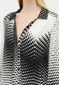 Black and white shirt with a V-neck, featuring a polka dot pattern that fades in size, button detail down the front, and a classic collar.