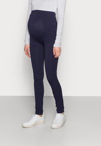 Maternity leggings in dark navy, made of stretch fabric. Features a high waistband for support and a slim fit. Worn with white sneakers.