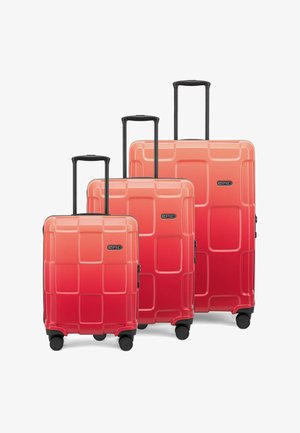 Drei sanft rot verlaufende Hartschalenkoffer mit einem quadratischen Muster, Teleskopgriffen und vier schwarzen Rädern.