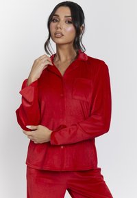 Rode corduroy pyjama set met een gekraagde knoopsluiting bovenkant met een patchzak en lange mouwen, in combinatie met bijpassende broeken.