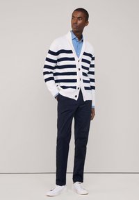 Cardigan bianco e blu a righe con collo sciallato, chiusura a bottoni, indossato sopra una camicia azzurra chiara e pantaloni scuri, abbinato a sneakers bianche.