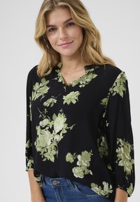 Blusa nera floreale con motivi di rose verdi e bianche, caratterizzata da scollatura a V e maniche a 3/4, realizzata in tessuto leggero e a costine.
