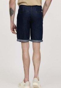Shorts en denim bleu foncé, avec des ourlets retroussés et un design classique à cinq poches. Présente une coupe droite et des coutures robustes.