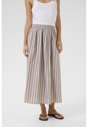 Falda maxi de rayas beige con rayas verticales blancas, cinturilla elástica y tejido ligero. Combinada con una camiseta sin mangas blanca y chanclas negras.