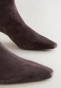 Botas de ante hasta el tobillo en gris oscuro con un diseño de punta afilada. La textura es suave, con un mínimo de costuras y una silueta elegante.