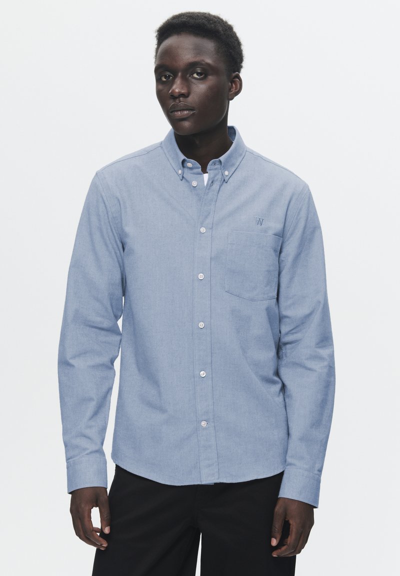Light blue button-up shirt made of a soft fabric, featuring a chest pocket and a small embroidered logo. Long sleeves and classic collar design.