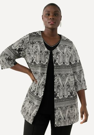 Schwarz-weißer Paisley-musterter Blazer mit Dreiviertelärmeln, offenem Frontdesign und strukturiertem Stoff. Getragen über einem schwarzen Oberteil.