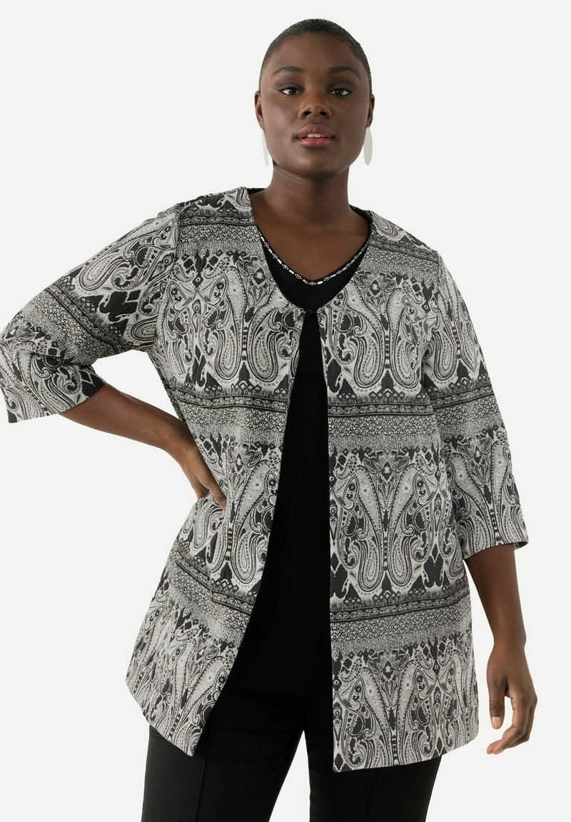 Schwarz-weißer Paisley-musterter Blazer mit Dreiviertelärmeln, offenem Frontdesign und strukturiertem Stoff. Getragen über einem schwarzen Oberteil.