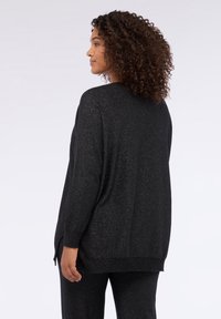 Top nero a maniche lunghe con glitter, vestibilità comoda, scollo tondo, polsini a costine e spacchi laterali all'orlo. Tessuto strutturato che conferisce brillantezza.