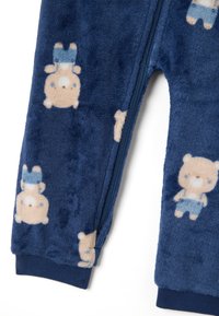 Pigiama in pile blu navy con motivi di orsi. Presenta una cerniera frontale e polsini a costine. Texture morbida, design giocoso con orsi dai colori chiari.