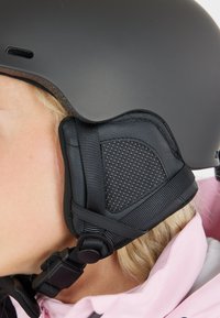 Black helmet with a smooth finish, padded black ear covers, and adjustable straps. Prominent ear padding features a textured pattern.