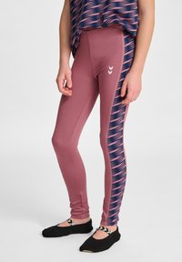 Legginsy w miękkim różowym kolorze z ciemnoniebieskim wzorzystym paskiem po boku; posiadają białe logo na przedniej części pasa. Czarne obuwie ze zapięciem.