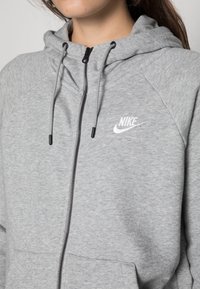 Felpa grigia con zip realizzata in materiale morbido, con logo Nike bianco, coulisse regolabile e tasche con zip.