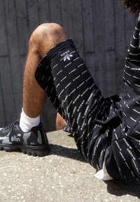 Svarta shorts med ett upprepat vitt "adidas"-logomönster i kombination med svarta och grå sneakers med en slät yta och vaddering.