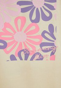 Kremasto tkanino krasijo velike rožnate in vijolične cvetlice z rdeče pikčastimi središči. Besedilo "Blooming Bliss" je vezeno v roza barvi.