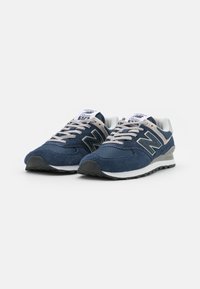 New Balance 574 tossud, millel on tumepunane samet ja võrgusilmast ülemine osa, hallid aktsendid, paeltega kinnitamine ja must kummist välistald.
