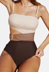 Bikini-Set mit beigem Bandeau-Oberteil, braunem Mittelteil und hochgeschnittenen, dunkelbraunen Unterteilen. Besitzt eine silberne Hardware-Akzent. Glatte Textur.