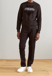 Sudadera negra con un gráfico de un tigre gris, combinada con pantalones negros y zapatillas blancas sobre un suelo de madera. Diseño simple y moderno.