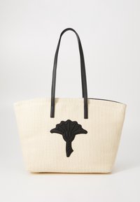 Sac fourre-tout beige en tissu tissé avec de longues poignées en cuir noir et un emblème de fleur stylisée noire centré à l'avant.