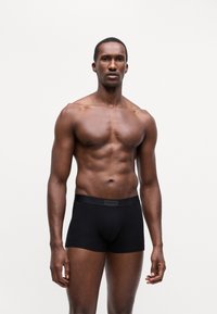 Sorte stretch bomull boxershorts med en myk midje som har "HUGO"-logoen, modellen viser en nøytral posisjon mot en ensfarget bakgrunn.