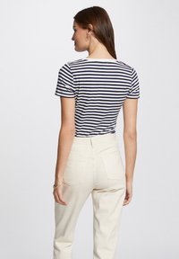 Striped t-skjorte i marineblå og hvit, kortermet, med rund hals og horisontalt mønster. Kombinert med lys beige høyt midje-bukser.