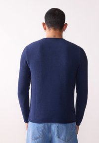 Marineblå strikket genser med lange ermer og rund hals, med strukturert stoff og figursydd design, parret med lyseblå denim.