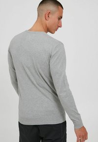Suéter gris claro con cuello redondo, mangas largas y puños y dobladillo de canalé, mostrado desde una vista lateral-posterior.