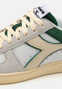 White sneakers with gray suede accents, green overlays, and cream laces. Features perforated details and a textured rubber sole.