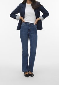 Mörkblå utsvängda jeans med hög midja, ihop med en vit t-shirt och en marinblå blazer. Svarta spetsiga klackar fulländar outfiten.
